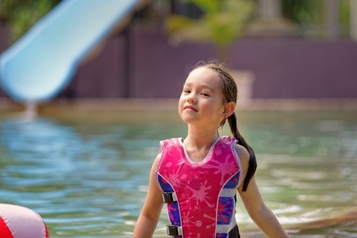 Young girl in a swimming pool playing with a ball wearing a swim vest - Australian Stock Image