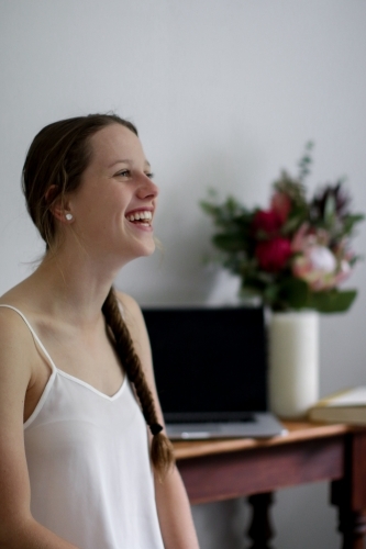 Young girl laughing inside in front of work desk - Australian Stock Image
