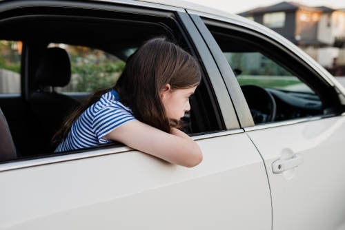 Young girl leaning out the open window of the family car parked in the driveway - Australian Stock Image