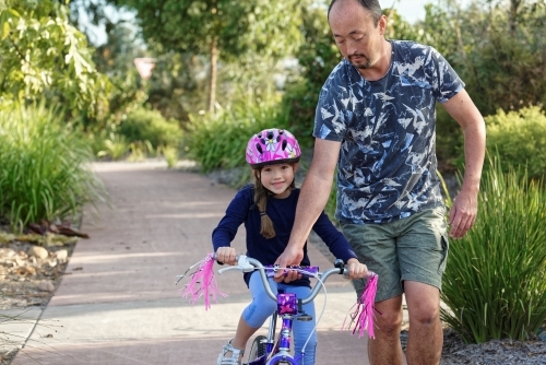 Young girl learning to ride her pushbike in the park with her dad - Australian Stock Image