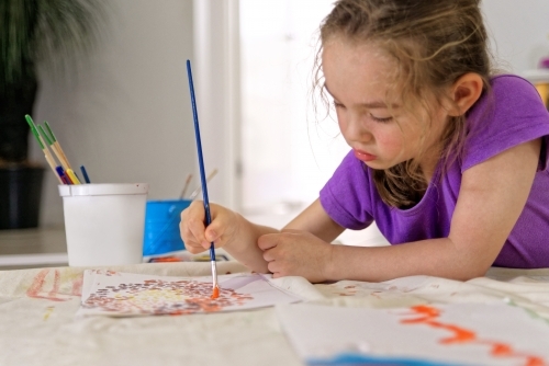 Young girl lying on the floor painting a dot picture with a paint brush - Australian Stock Image