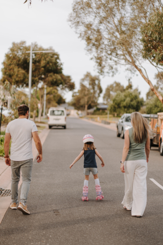 Young girl on roller blades with her parents on the street. - Australian Stock Image