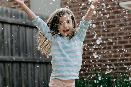 Young girl playing in home backyard splashing water - Australian Stock Image