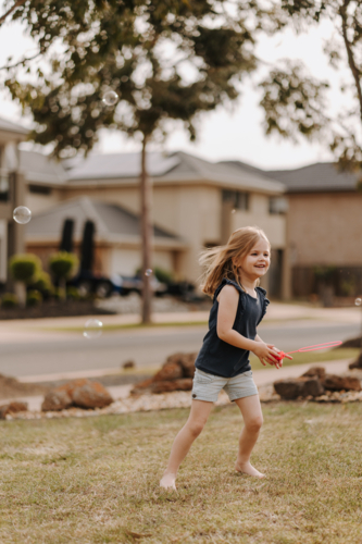 Young girl playing with bubbles in front yard. - Australian Stock Image