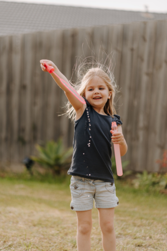 Young girl playing with bubbles inside their yard. - Australian Stock Image