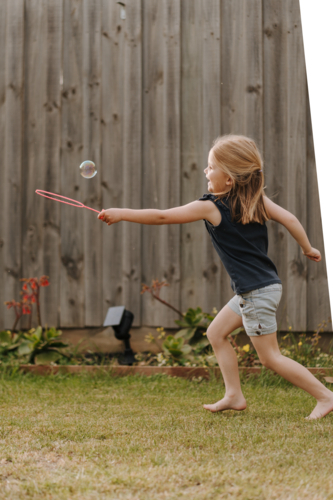 Young girl playing with bubbles inside their yard. - Australian Stock Image