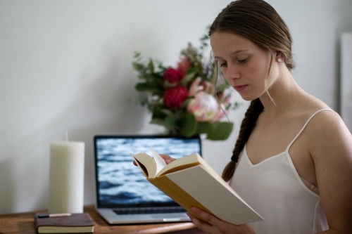 Young girl reading a book indoors by her work desk - Australian Stock Image