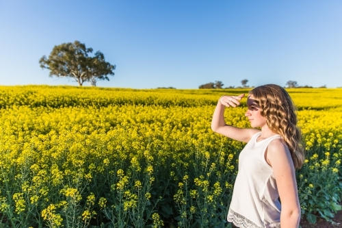 Young girl shielding face from sun looking out at canola farm field
