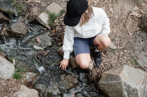 Young girl sitting by a creek touching the water - Australian Stock Image
