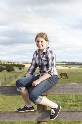 Young girl sitting on fence at horse riding farm - Australian Stock Image