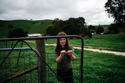 Young girl standing behind the metal farm gate - Australian Stock Image