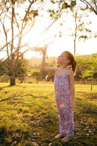 Young girl standing in a field looking up at flowers - Australian Stock Image