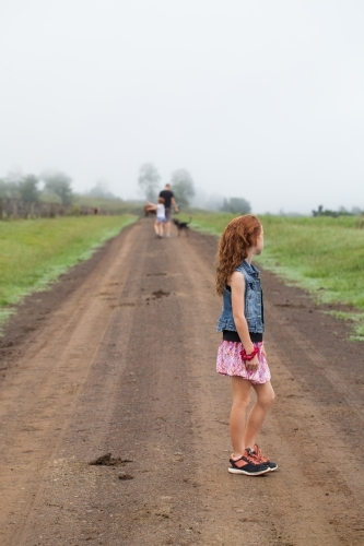 Young girl standing on a dirt track with family in the distance