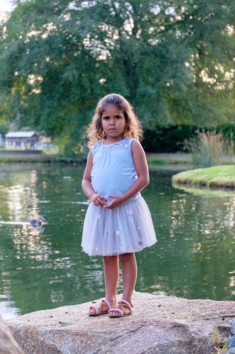 Young girl standing on a flat rock along the lakeside. - Australian Stock Image