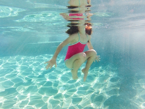 Young girl swimming underwater at a pool - Australian Stock Image