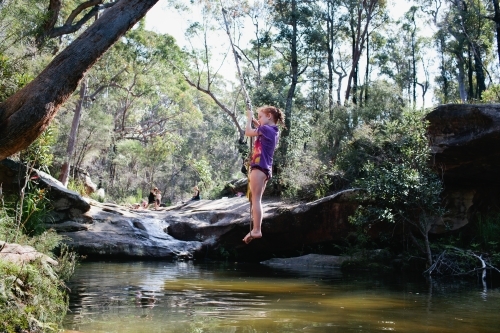 Young girl swinging on a rope swing at a waterhole