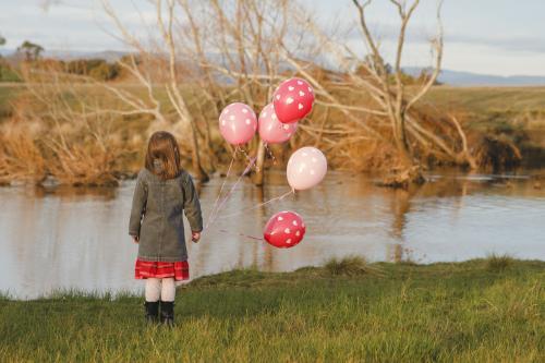 Young girl with a bunch of pink birthday balloons beside a river