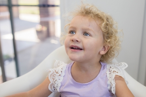 Young girl with blonde curls sitting in chair - Australian Stock Image