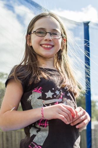 Young girl with glasses standing on trampoline smiling