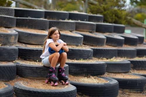 young girl with long hair sitting outdoors wearing roller skates - Australian Stock Image