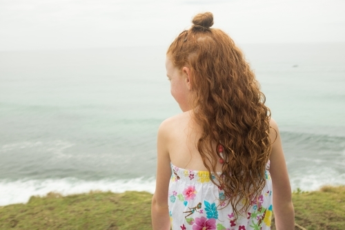 Young girl with long red hair watching the ocean