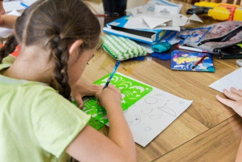 Young girls are creating artwork, drawing Manga and stencilling at the table - Australian Stock Image
