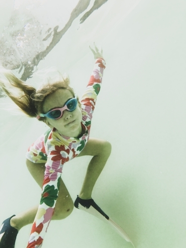 Young girls swimming underwater in pool wearing floral swimsuit, goggles and fins