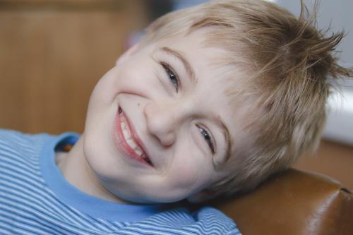 Young happy boy leaning on a leather couch smiling - Australian Stock Image