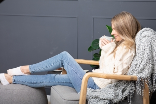 Young lady relaxing drinking hot chocolate or coffee on a cold winters day - Australian Stock Image