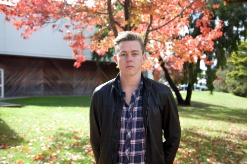 Young male with serious expression standing outdoors - Australian Stock Image