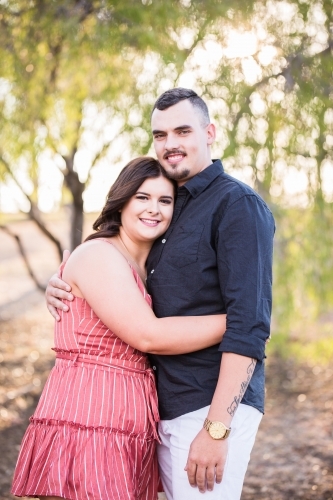 Young man and woman standing smiling with arms around each other - Australian Stock Image