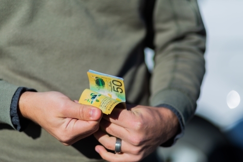 Young man holding cash standing in front of car paying up front - Australian Stock Image