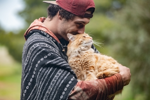 Young man interacting with ginger pet cat - Australian Stock Image