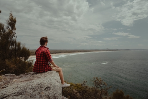 Young man relaxing at a lookout overlooking the beach and ocean at Evans Head. - Australian Stock Image