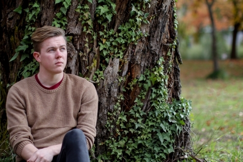 Young man sitting outdoors at the base of a tree contemplating life