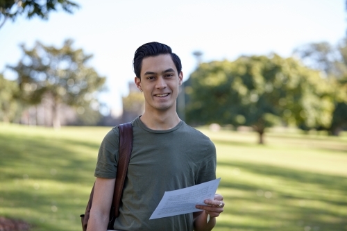 Young man smiling outdoors holding his music paper - Australian Stock Image