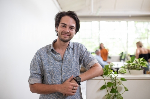 Young man standing, smiling in white office - Australian Stock Image