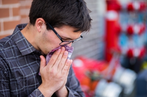 Young man suffering from hay fever using a hanky to blow his nose - Australian Stock Image