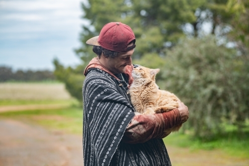 Young man talking and interacting to his ginger cat outdoors. - Australian Stock Image