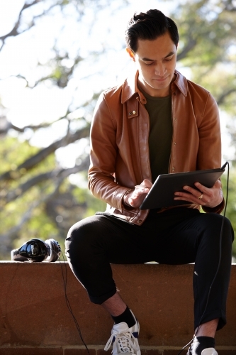 Young man with dark hair outside holding device with headphones at park - Australian Stock Image