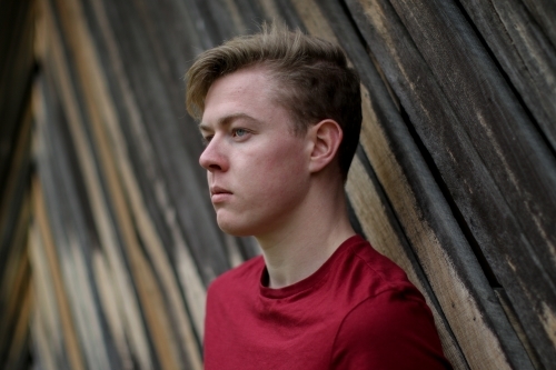 Young melancholy caucasian man modelling in front of a wooden panelled background - Australian Stock Image