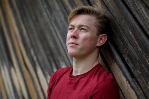 Young melancholy caucasian man modelling in front of a wooden panelled background - Australian Stock Image