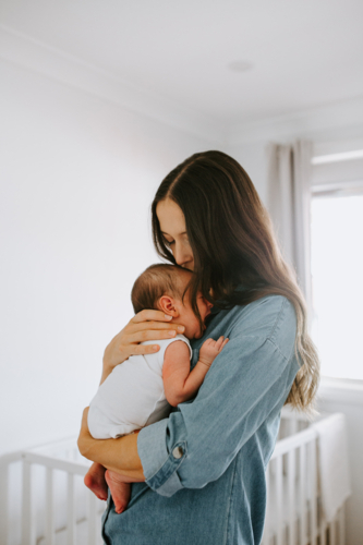 Young mother carrying newborn baby boy in the room - Australian Stock Image
