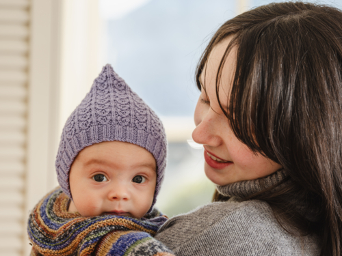 Young mother holding baby wearing beanie inside home - Australian Stock Image