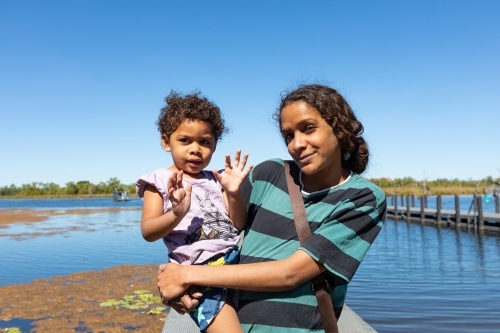 young mother holding daughter on her hip with water in background