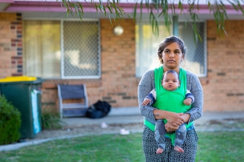 Young mother with baby in wrap out front of their home