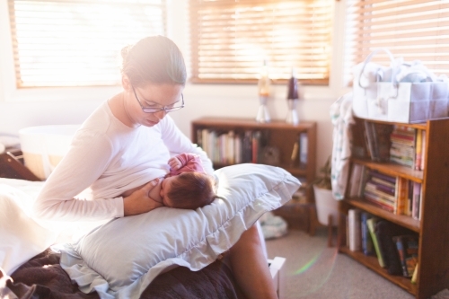 Young mum in bedroom breastfeeding content newborn baby with light flare - Australian Stock Image