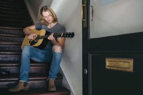 Young musician playing guitar on the stairs