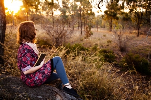 Young person holding a notebook looking away, outside in nature - Australian Stock Image