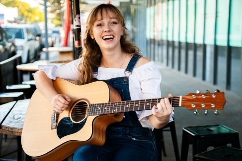 Young person playing guitar outside cafe - Australian Stock Image